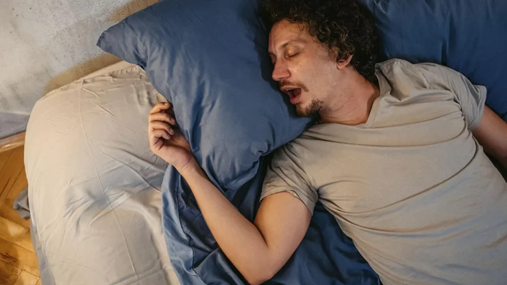 man sleeping on blue pillows with mouth open, appearing to snore peacefully