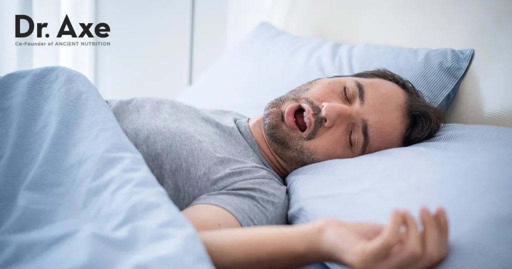 man sleeping with mouth open in a cozy bed, blue bedding, appearing to snore peacefully