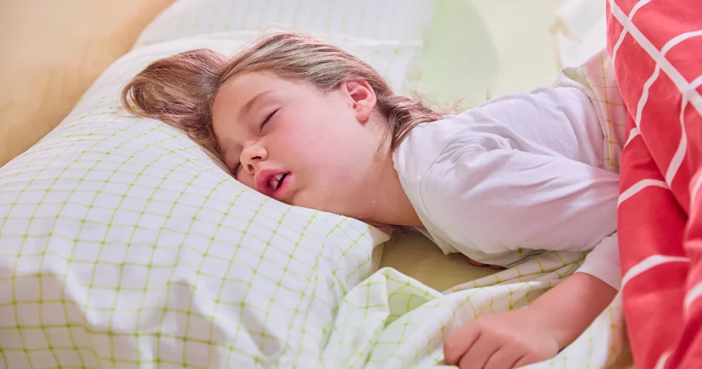 young girl peacefully sleeping on a pillow with a green checkered pattern and a cozy blanket nearby